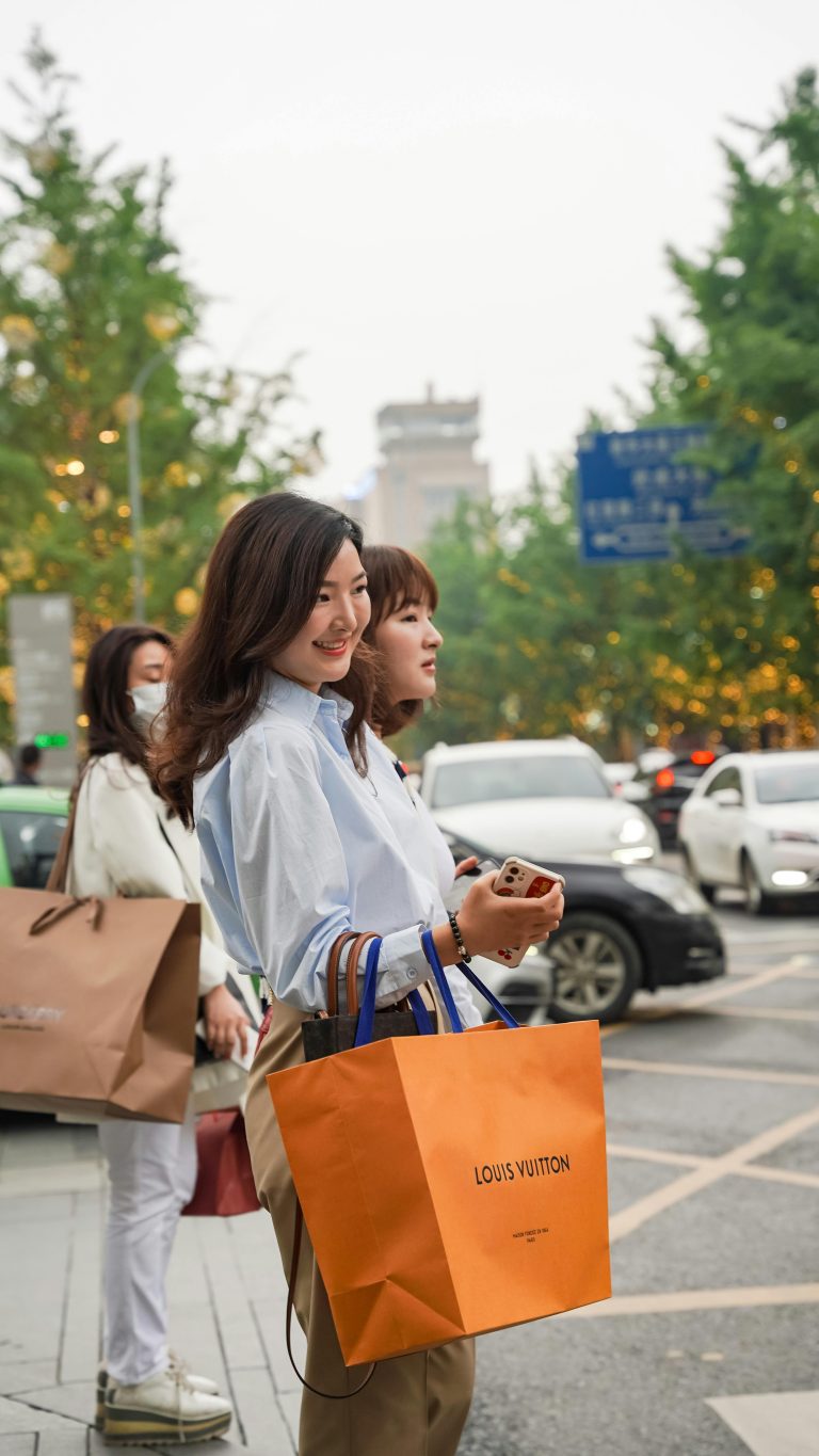 Asian women with shopping bags outdoors on a busy city street.