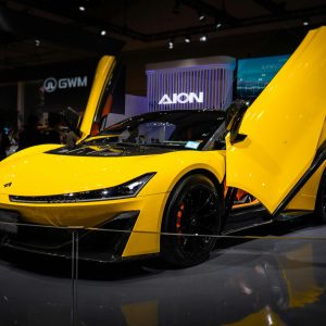 Yellow sports car with gullwing doors showcased at an indoor auto exhibition.