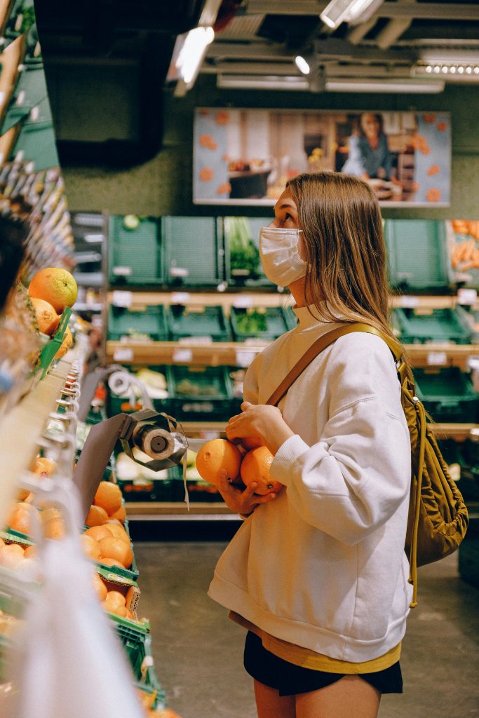 Woman in a mask selects fresh oranges in a supermarket, emphasizing hygiene and protection.