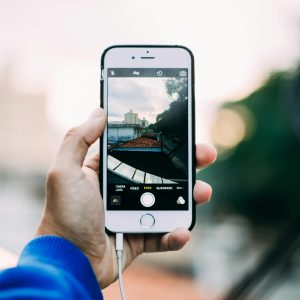Close-up of a hand holding a smartphone while capturing a cityscape outdoors.